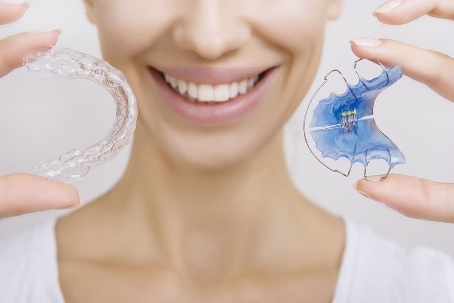 Clear Invisalign aligner beside traditional metal braces