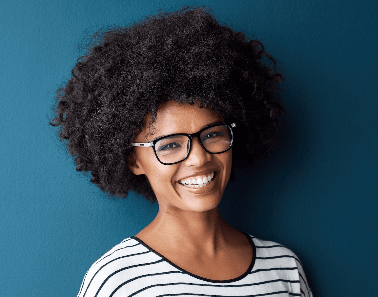 Young woman with natural hair and glasses smiling brightly after Zoom whitening at Advanced Dental Care Leesburg